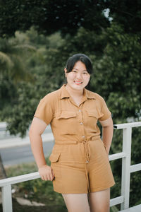 Portrait of smiling young woman standing against trees