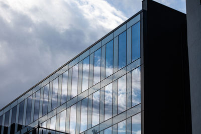 Low angle view of glass building against cloudy sky