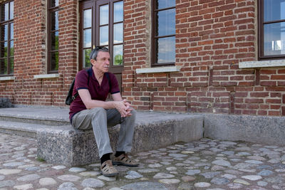 Full length portrait of man sitting against brick wall