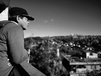 Man looking away while standing by railing against sky