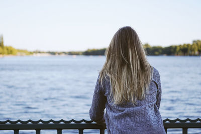 Rear view of woman looking at lake against clear sky