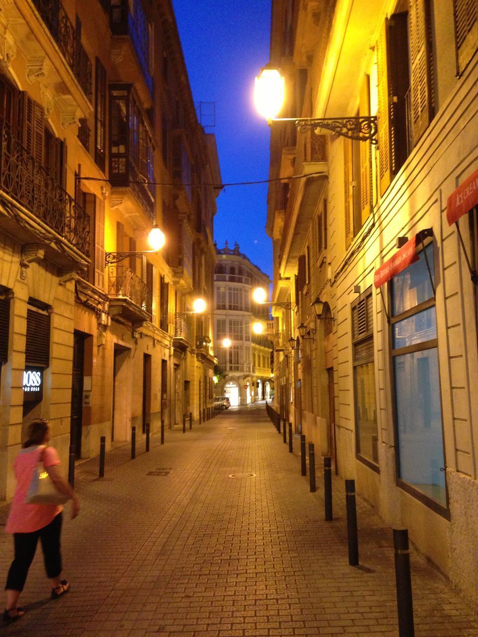 REAR VIEW OF PEOPLE WALKING ON ILLUMINATED STREET AMIDST BUILDINGS