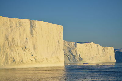 Scenic view of frozen sea with icebergs against clear sky in midnight sun