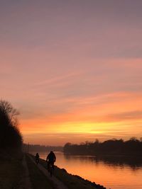 Silhouette people on lakeshore at sunset