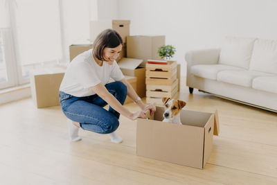 Smiling woman with dog in box crouching at home