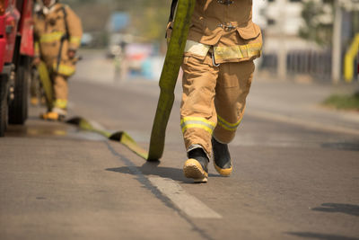 Low section of firefighter arranging fire hose on road