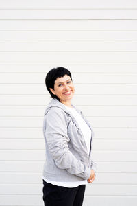 Portrait of a smiling young woman standing against wall