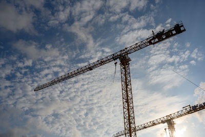 Low angle view of cranes at construction site against sky