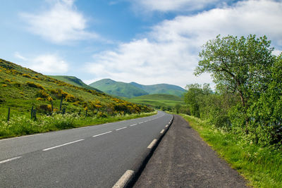 Empty road along trees and mountains against sky