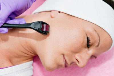 Close-up of woman lying down with while beautician using cosmetic roller on face at spa