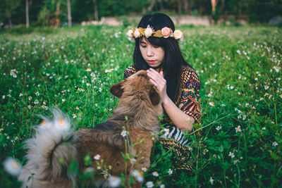 Woman wearing flowers while sitting with dog on field 