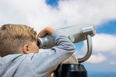 Rear view of boy looking through binoculars against sky