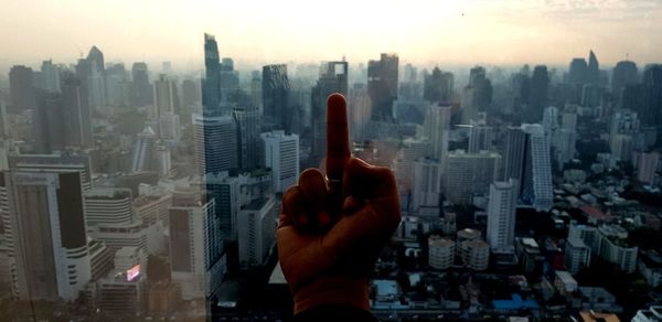 Cropped hand showing middle finger against cityscape 