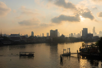 Scenic view of river by buildings against sky during sunset