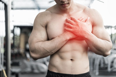 Midsection of shirtless muscular man suffering from chest pain in gym