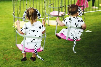 Rear view of girls in dalmatian dog costumes sitting on swing at park