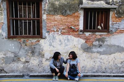 Full length of young couple sitting on window of building