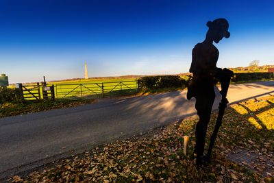 Man standing on road against clear blue sky