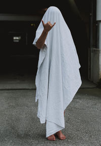 Woman gesturing while standing covered by white textile on footpath