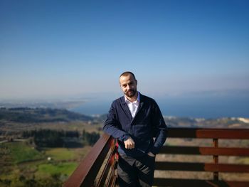 Portrait of young man standing against railing