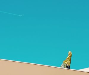 Low angle view of man covered with gold foil standing against blue sky