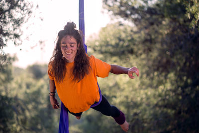 Young girl acrobat. practicing aerial silks. woman doing circus stunts with clothes in the forest. balance hip lock.