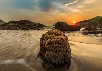 Rocks on beach against sky during sunset