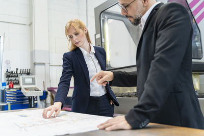 Businessman and businesswoman looking at plan on table in factory