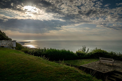 Empty bench by sea against sky