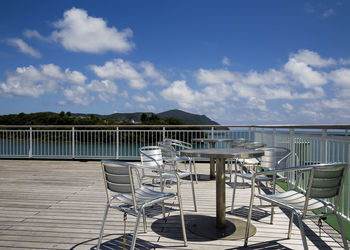 Chairs on railing by lake against sky
