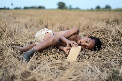 Boy using mobile phone while lying on field at farm