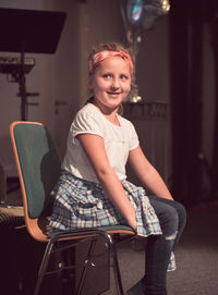 Smiling girl looking away while sitting on chair at home