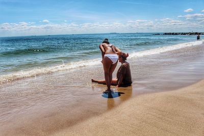 Woman sitting on beach against sea against sky