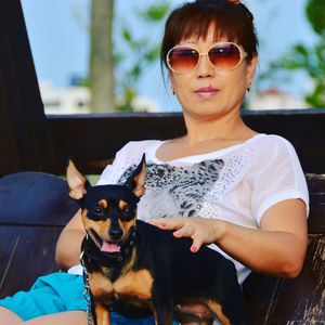 Woman sitting with miniature pinscher on wooden swing at yard