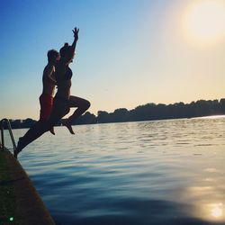 Full length of friends jumping over lake against clear sky