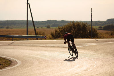 Back view of professional cyclist in activewear and helmet riding bike on road during morning time.