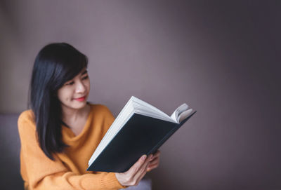 Woman reading book against wall at home