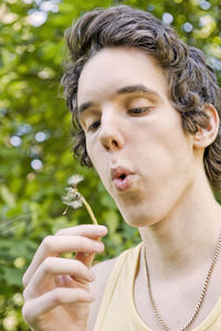 Low angle view of teenage boy blowing dandelion 