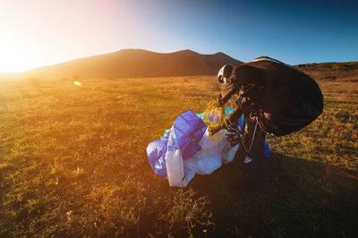 Rear view of woman sitting on rock against sky during sunset