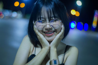 Portrait of smiling woman with hands on chin standing outdoors at night