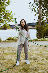 Full length portrait of confident young woman holding garden hose