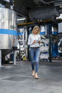 Young businesswoman using digital tablet while walking in factory