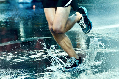 Low section of man running on wet road