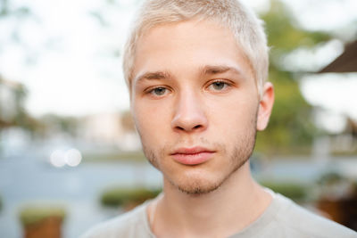 Handsome young man with blond short cut hairstyle smiling over city urban background outdoor