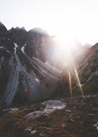 Scenic view of sun shining over mountains against sky