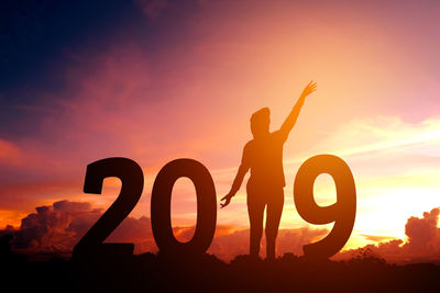 Silhouette woman with arms raised representing new year against sky during sunset