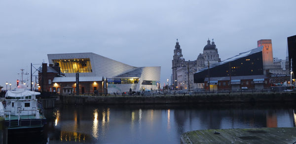 Illuminated buildings by river against sky in city