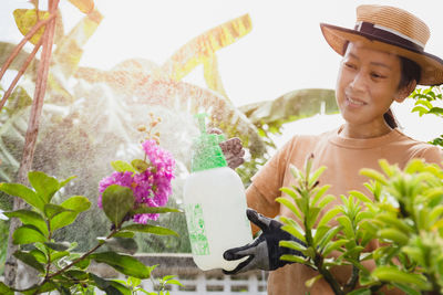 Beautiful asian woman in hat watering plant by foggy spray bottle in garden. 