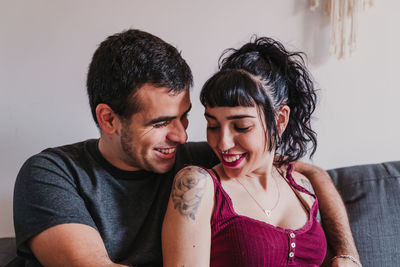 Smiling male embracing female while sitting on sofa at home