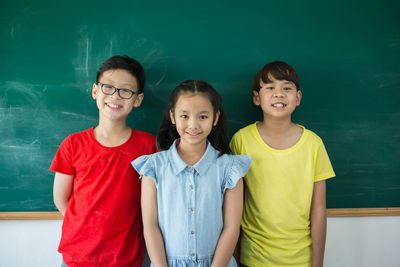 Portrait of smiling students standing against blackboard in classroom